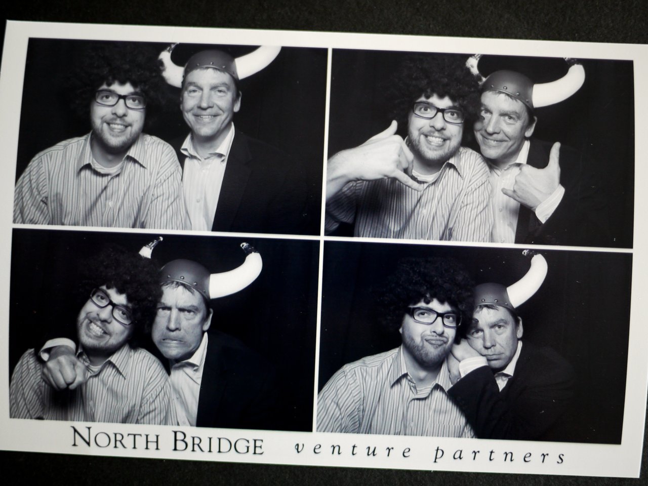 Two men in costumes pose playfully in a photo booth, wearing a wig, glasses, and a Viking helmet.