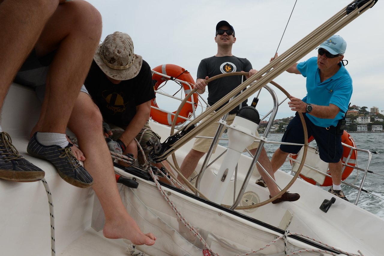 Four people are actively sailing a boat, adjusting ropes and steering while leaning on the tilted deck.