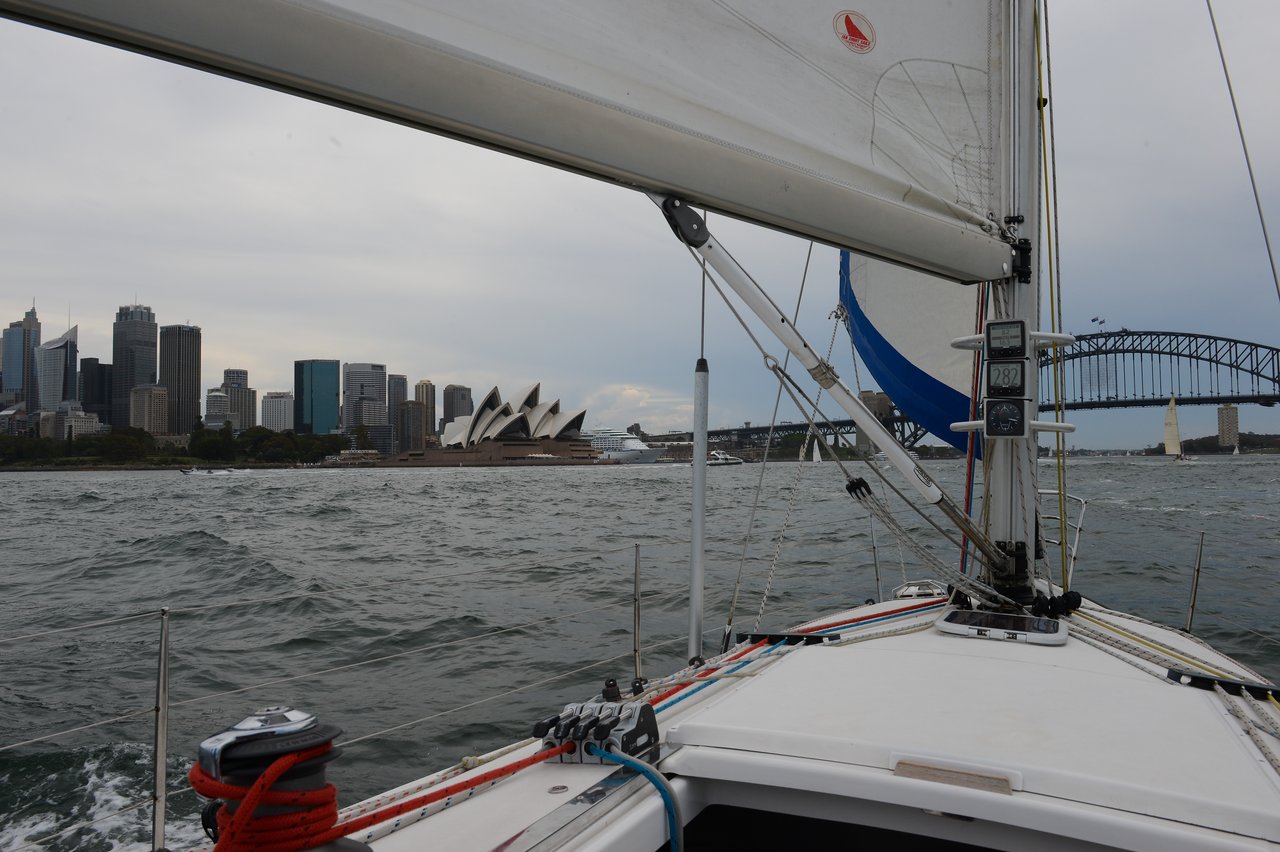 View from a sailboat, showing the Sydney Opera House and city skyline on the left and the Harbour Bridge on the right.