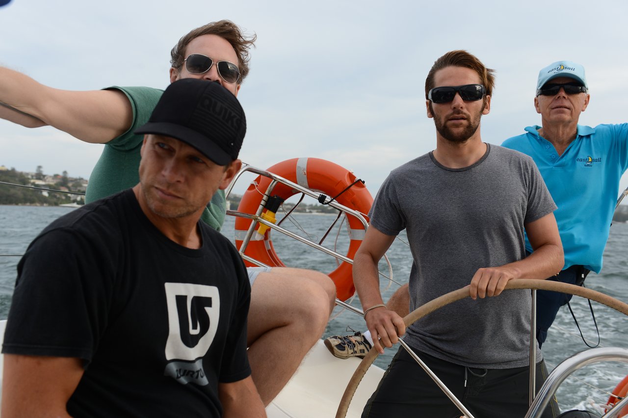 Four men are on a sailboat, with one steering the wheel.