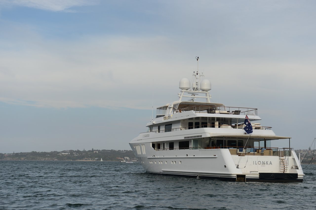 A large white luxury yacht named "ILONKA", with multiple decks, satellite domes, and an Australian flag waving at the stern.