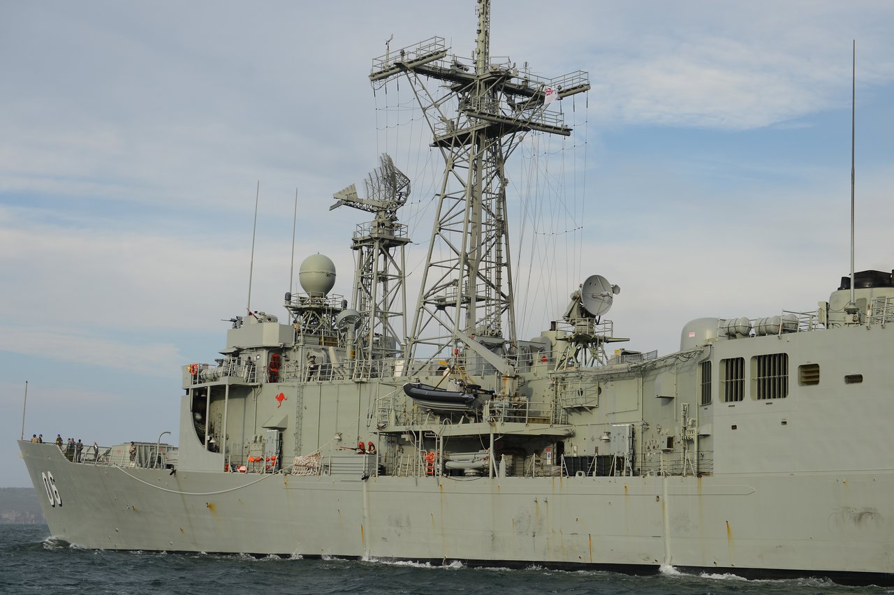 A large gray military ship with radar equipment and antennas, and crew members visible on deck.