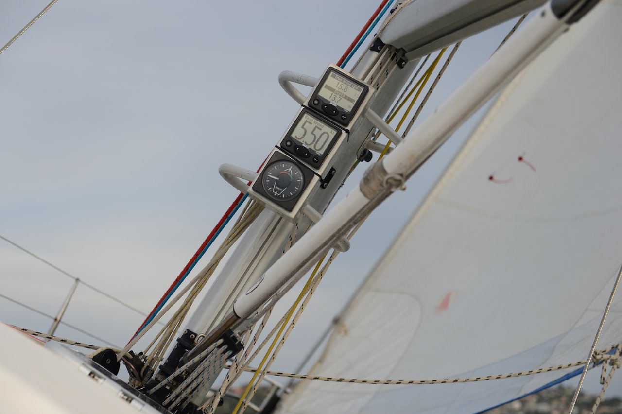 A close-up view of a sailboat's mast shows digital instruments displaying speed and wind data.