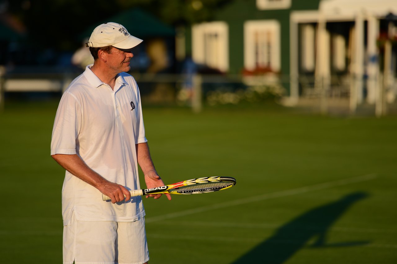A tennis player in a white outfit holds a racket on a grass court, preparing for the next play.