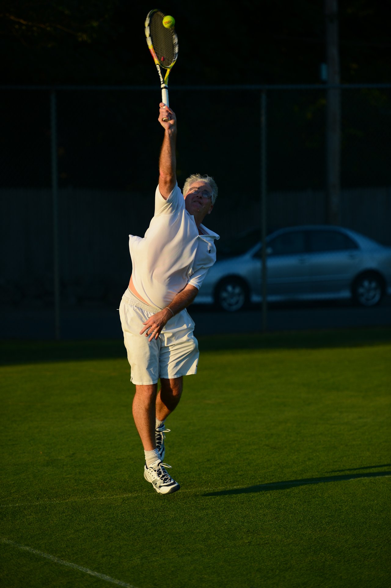 A tennis player in white clothing serves the ball on a grass court.