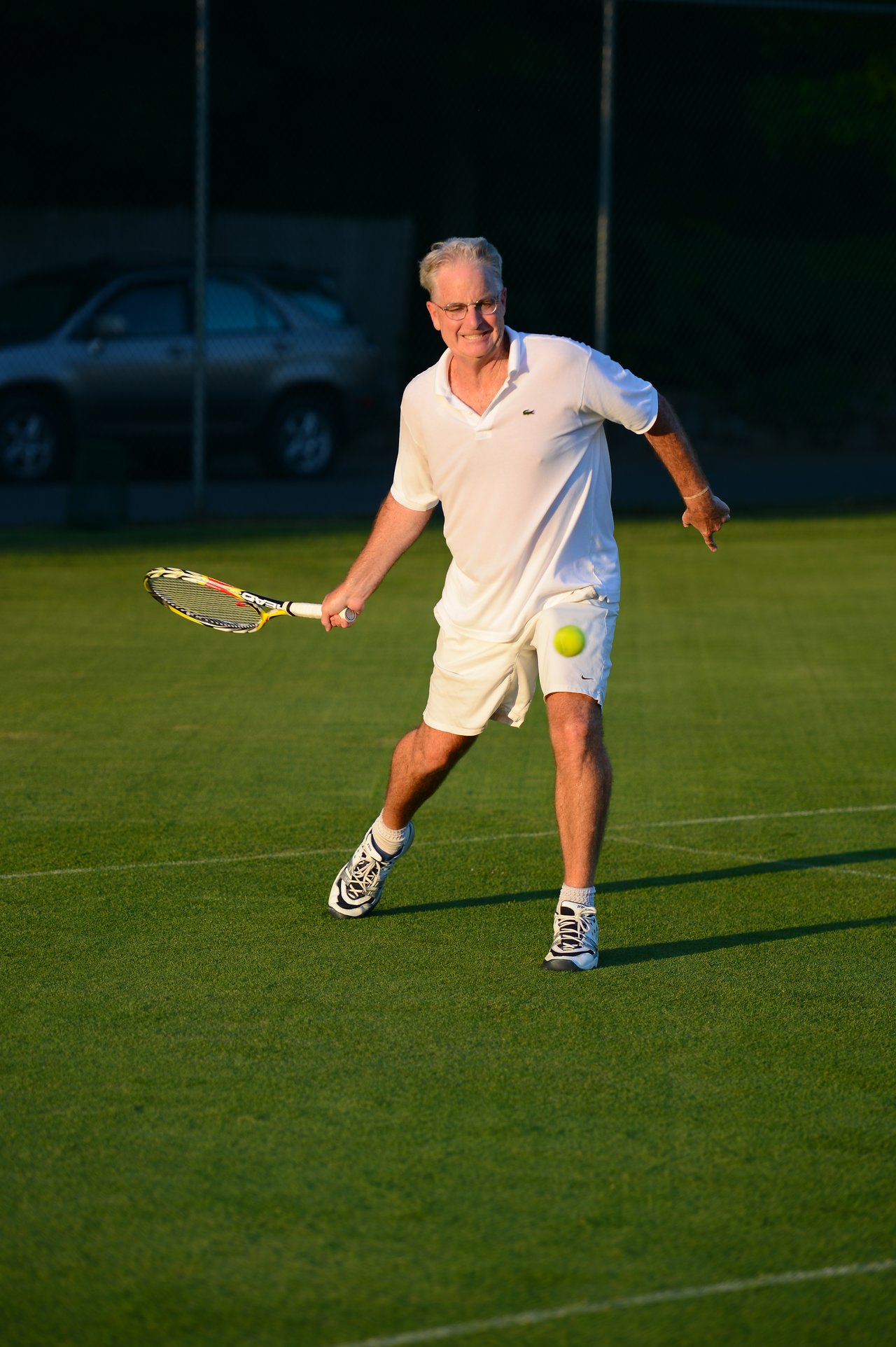 A man in white sportswear prepares to hit a tennis ball with his racket on a grass court.