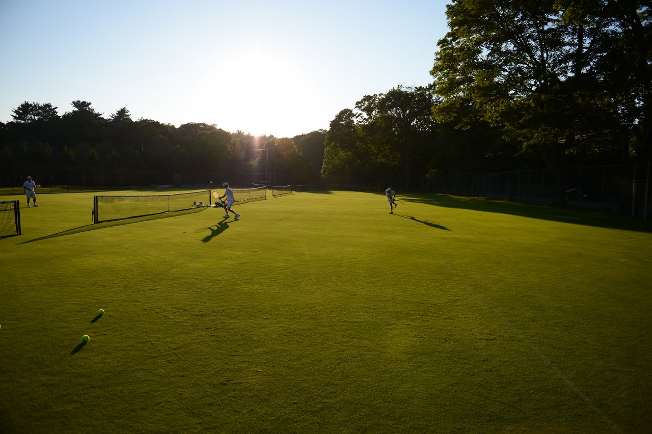Two people play tennis on a grass court, with one preparing to hit the ball.