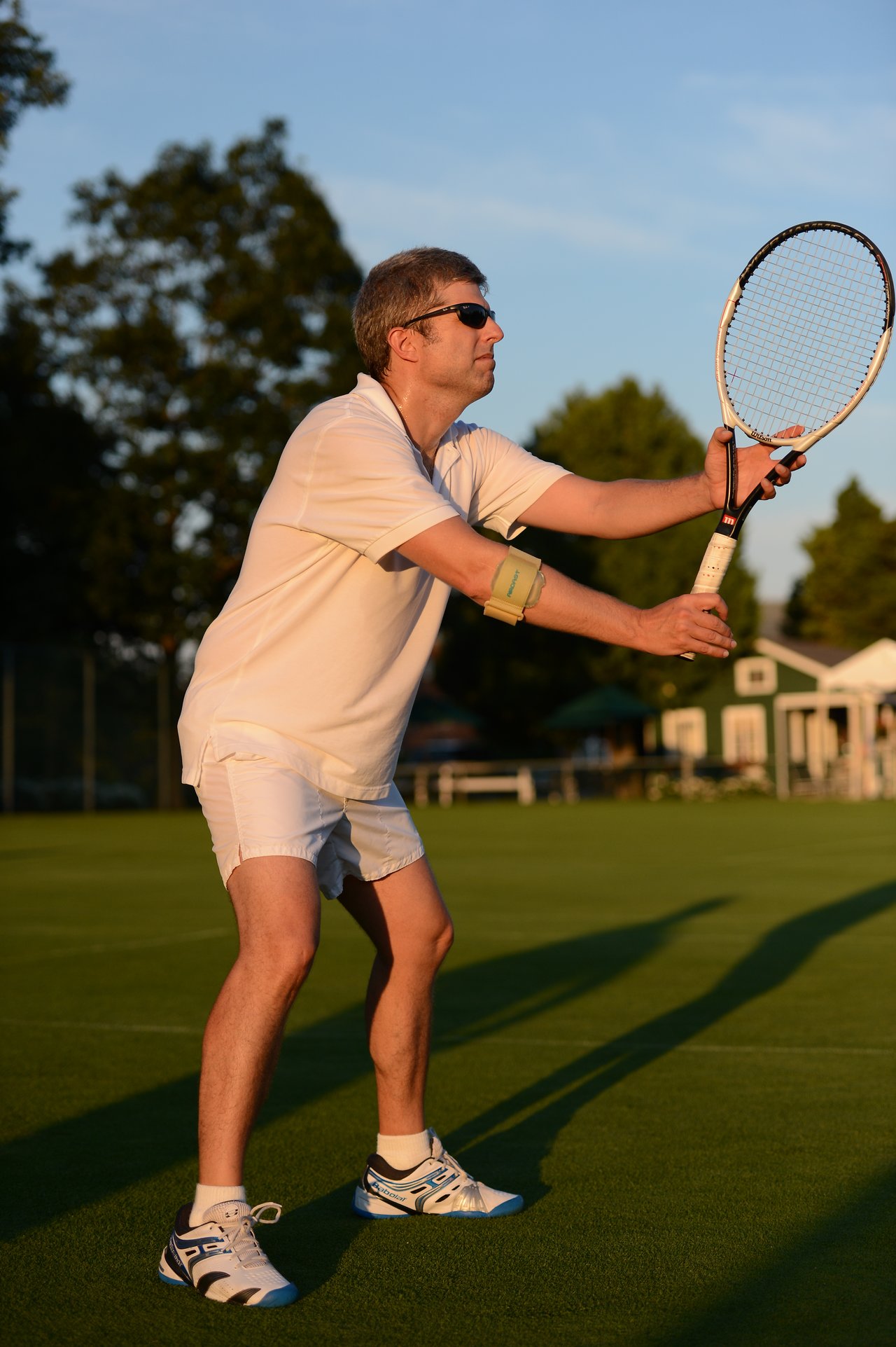 A man in tennis attire holds a racket and prepares to hit the ball on a grass court.