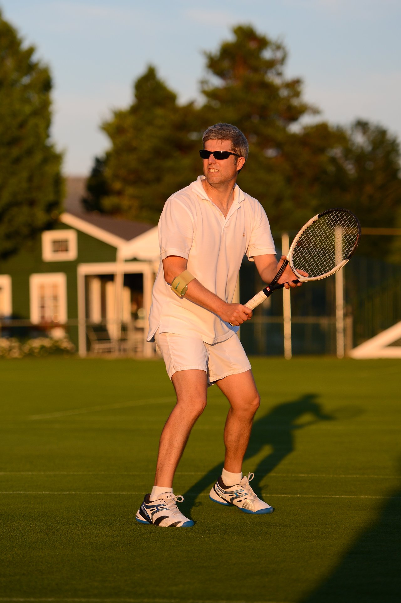 A man in white tennis attire holds a racket and prepares to hit the ball on a grass court.