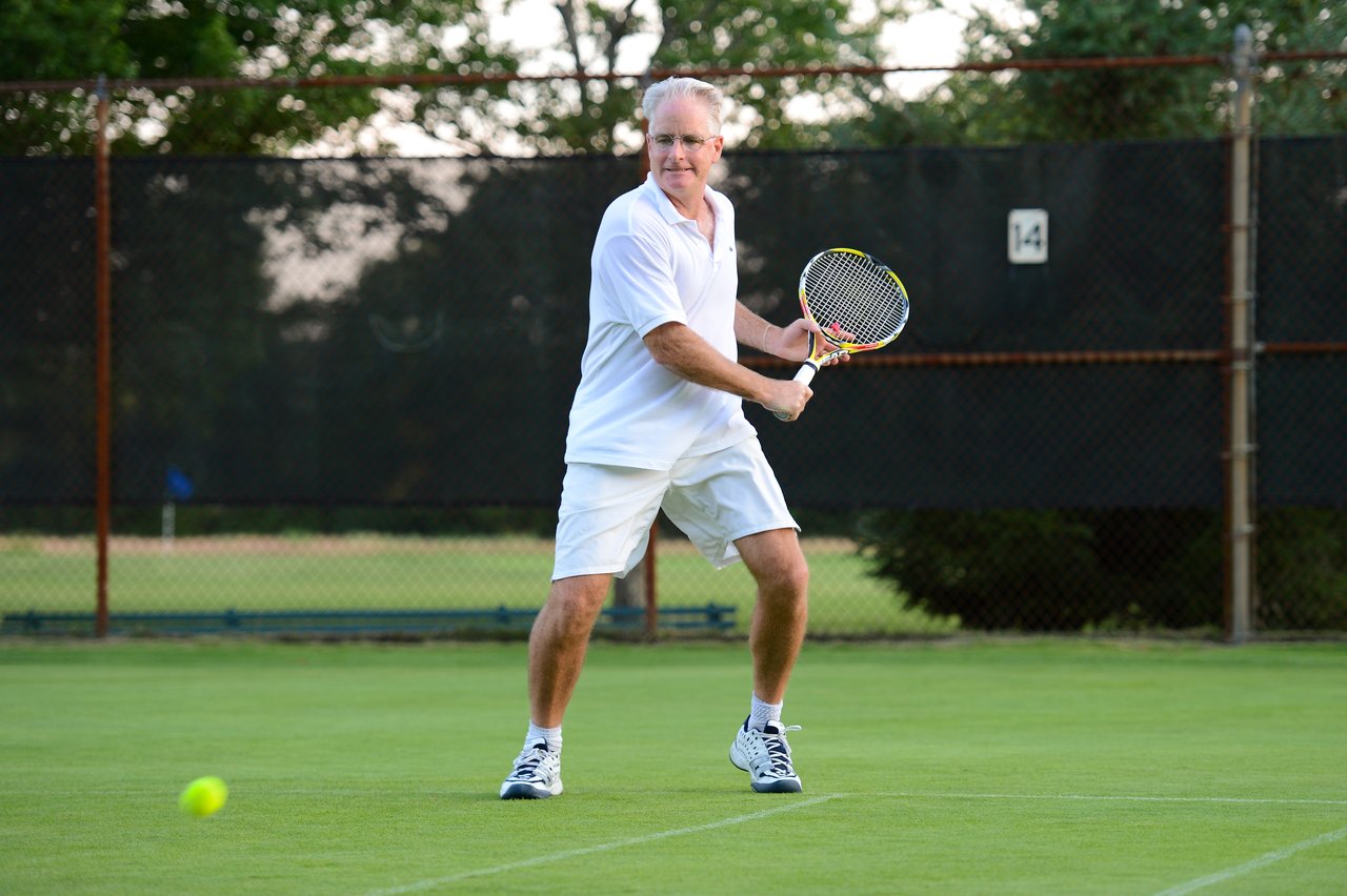 A man in white sportswear prepares to hit a tennis ball with a racket on a grass court.