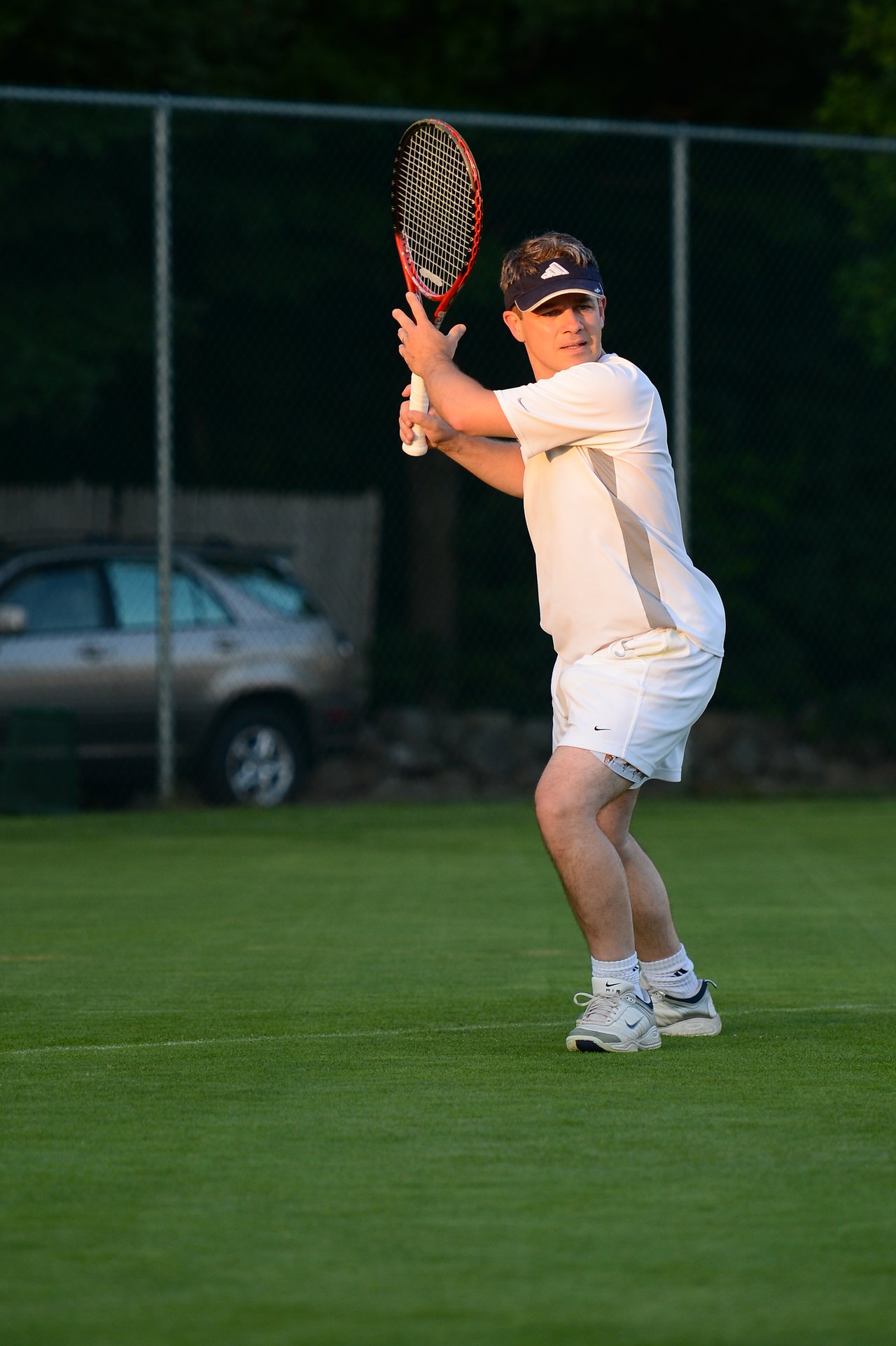 A tennis player in white prepares to hit a backhand shot on a grass court.