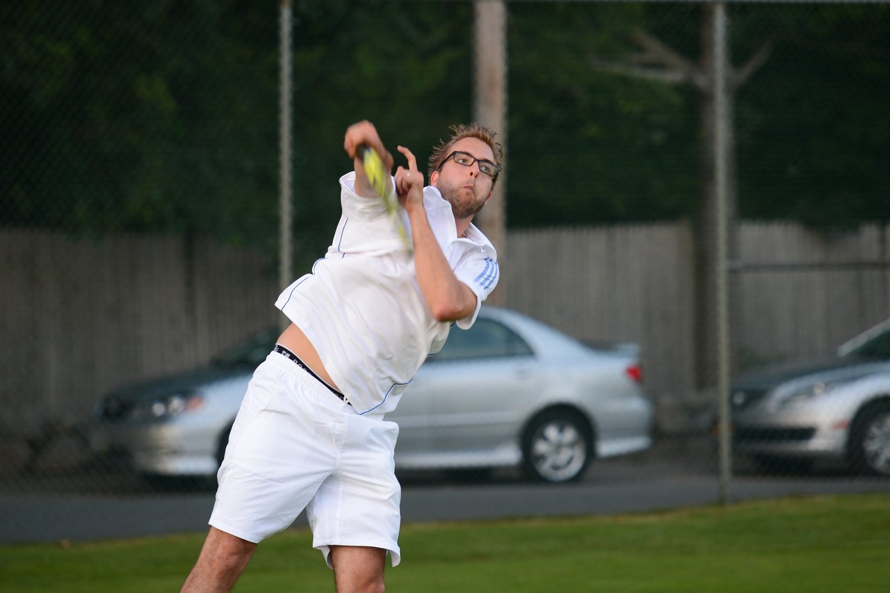 A tennis player in white clothing serves the ball during a match on an outdoor court.