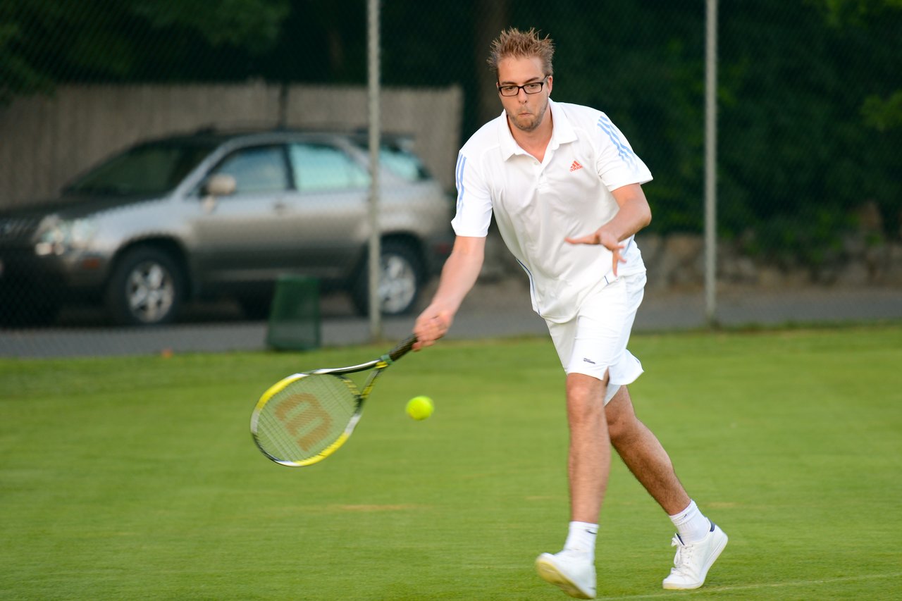A tennis player in a white outfit prepares to hit a ball with a racket on a grass court.