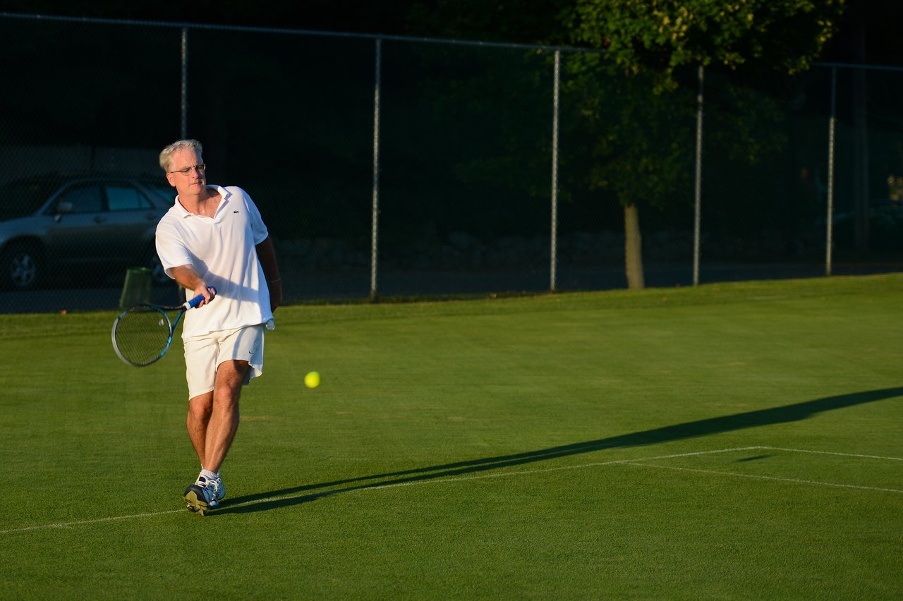 A man in white sportswear hits a tennis ball with a racket on a grass court.