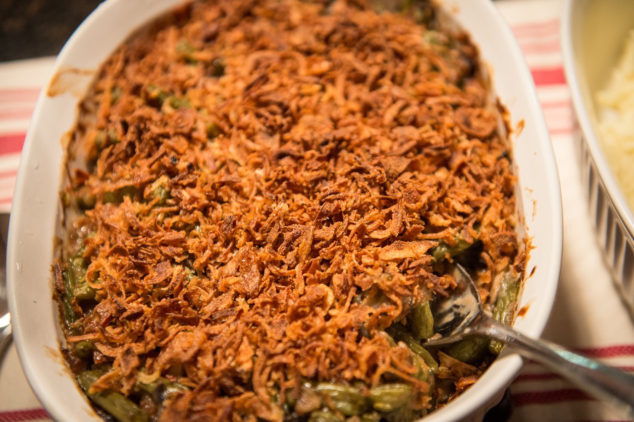 A dish of green bean casserole with a crispy fried onion topping, served in a white baking dish.