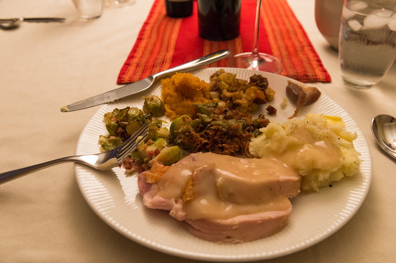 A plate of Thanksgiving food with turkey, mashed potatoes, Brussels sprouts, stuffing, and other side dishes on a table.