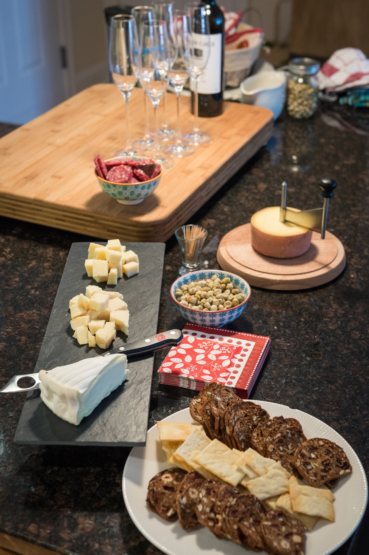 A Thanksgiving appetizer spread with cheese, crackers, salami, nuts, and wine glasses on a kitchen counter.
