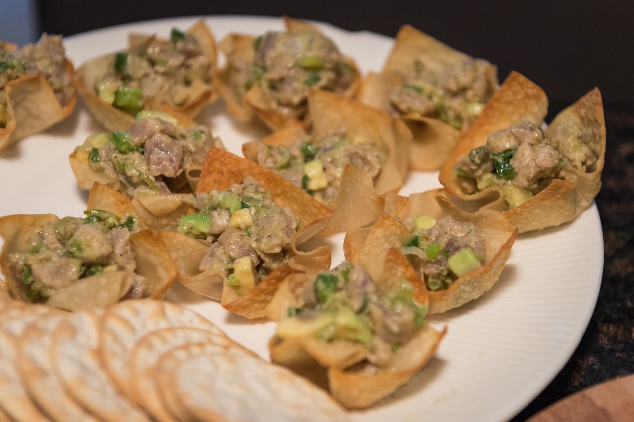 A plate of crispy wonton cups filled with a creamy mixture of diced meat, avocado, and green onions.