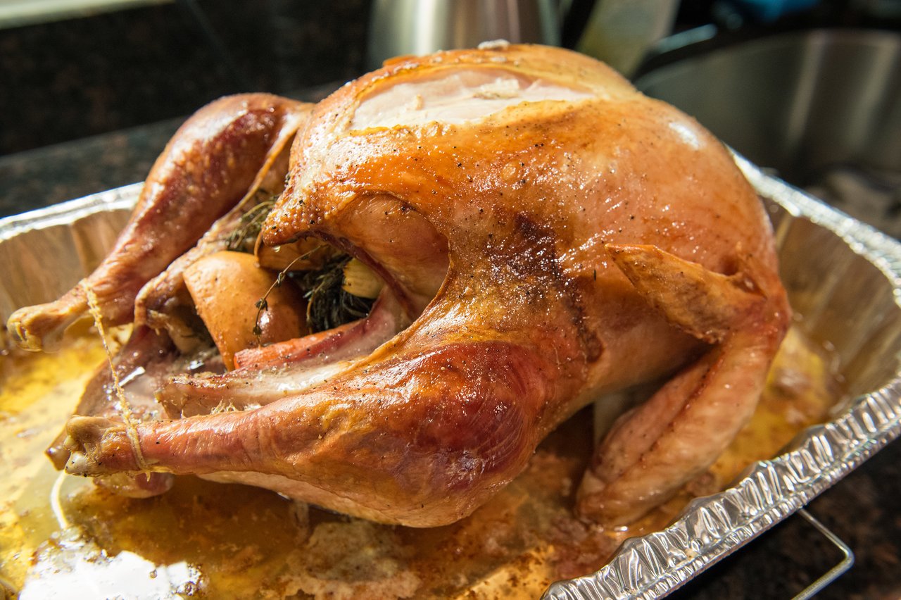 A roasted turkey with stuffing sits in a foil tray, ready to be served for Thanksgiving dinner.