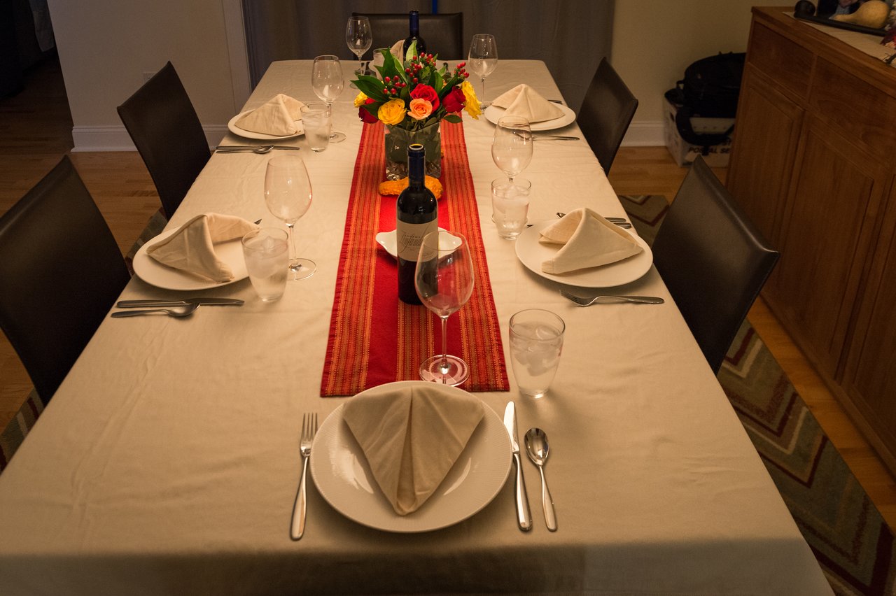A dining table set for Thanksgiving with folded napkins, plates, wine, and a floral centerpiece.