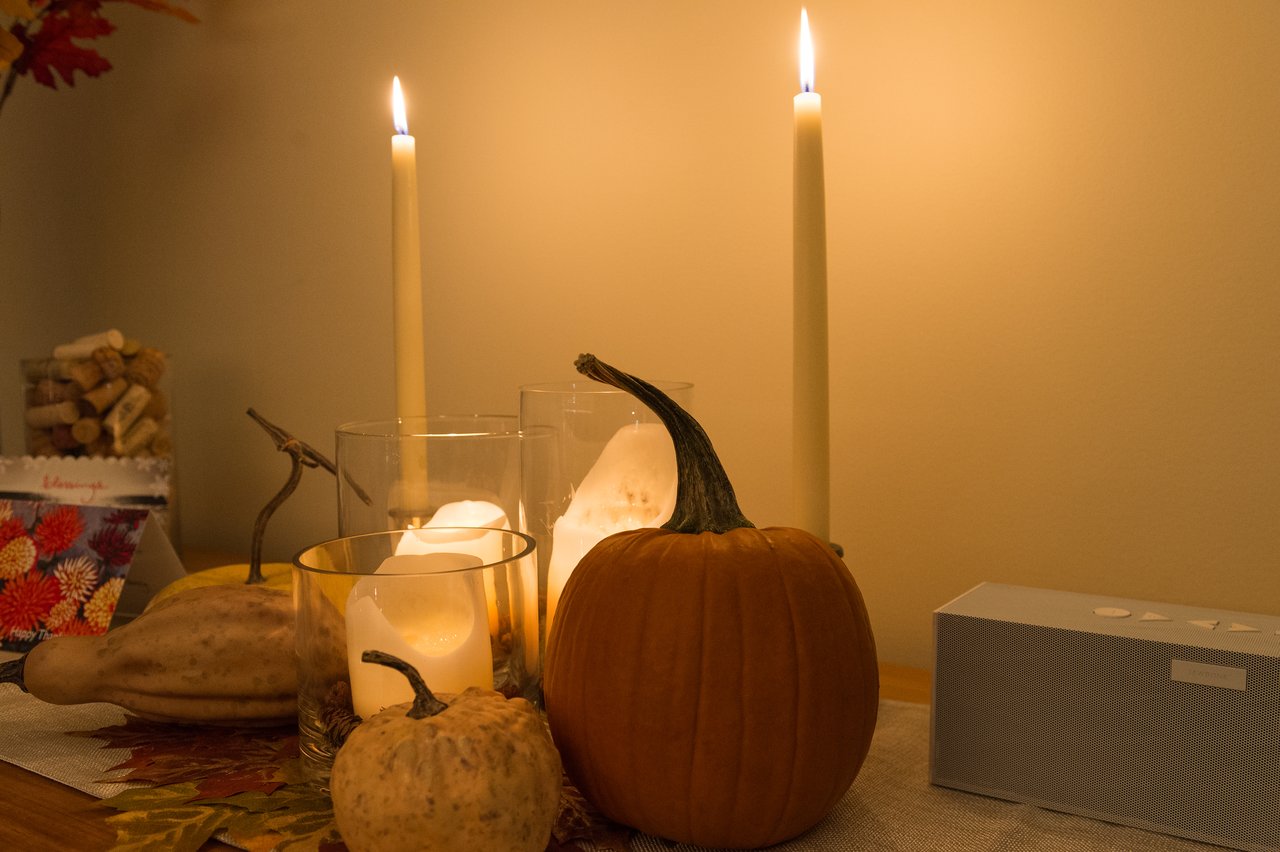 A Thanksgiving table with pumpkins, candles, and two lit tall candles creating a warm, festive atmosphere.