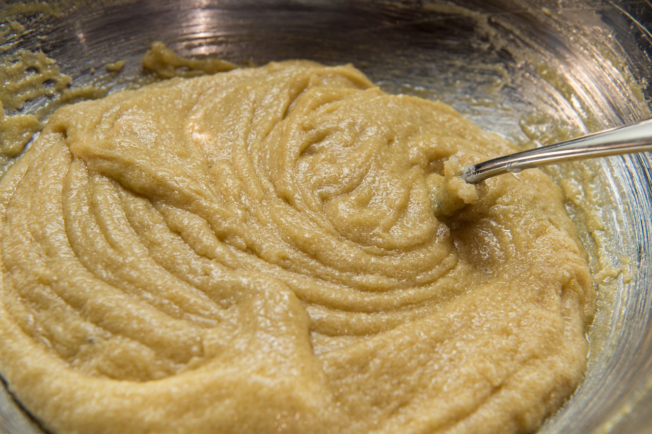 A metal spoon stirs thick cookie batter in a mixing bowl.