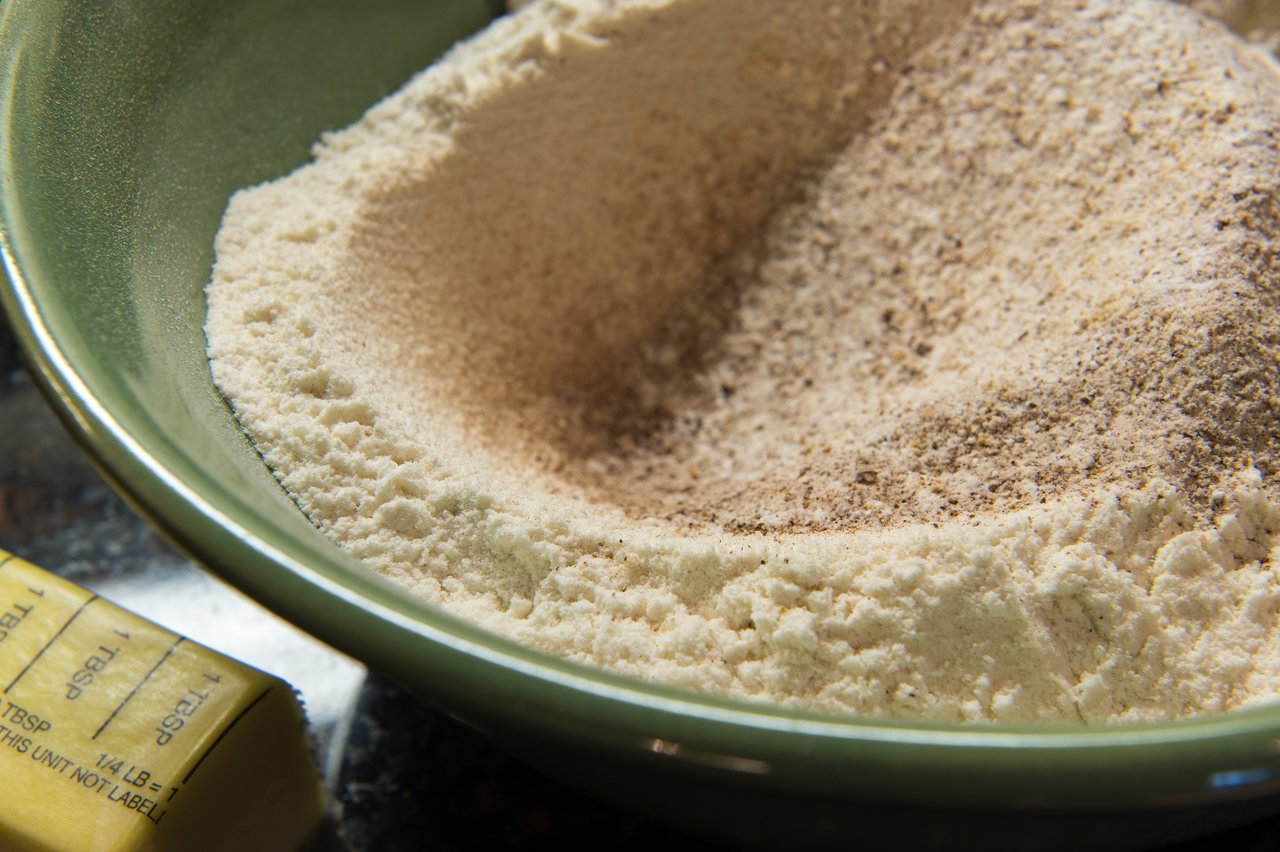 A green bowl filled with flour and spices, with a stick of butter nearby, for baking carrot cake cookies.