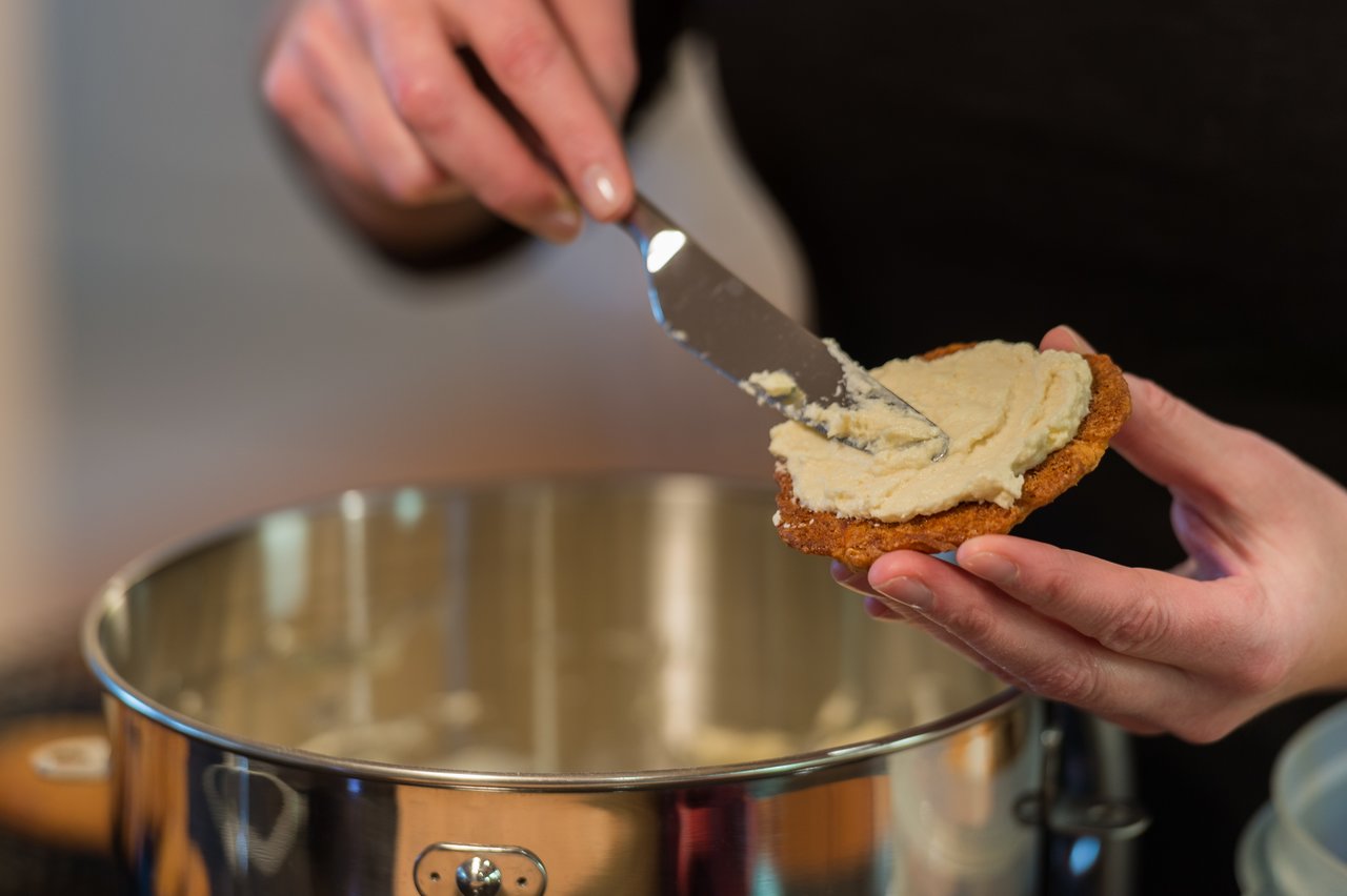 A person spreads frosting on a carrot cake cookie using a spatula, with a mixing bowl in the background.