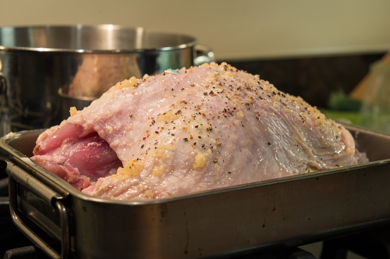 Raw turkey seasoned with garlic and pepper in a roasting pan, ready to be cooked.