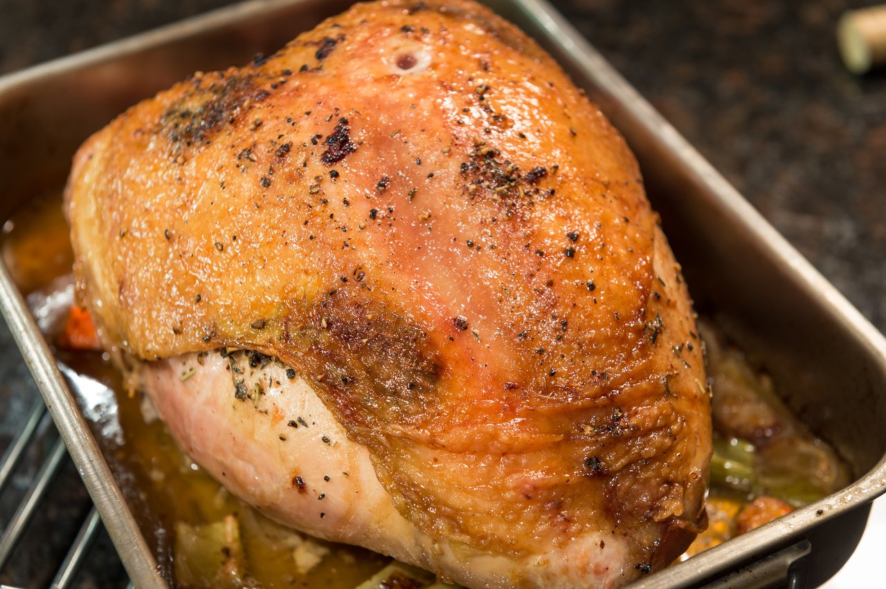 A roasted turkey breast with crispy, golden skin sits in a baking pan with juices and seasonings.