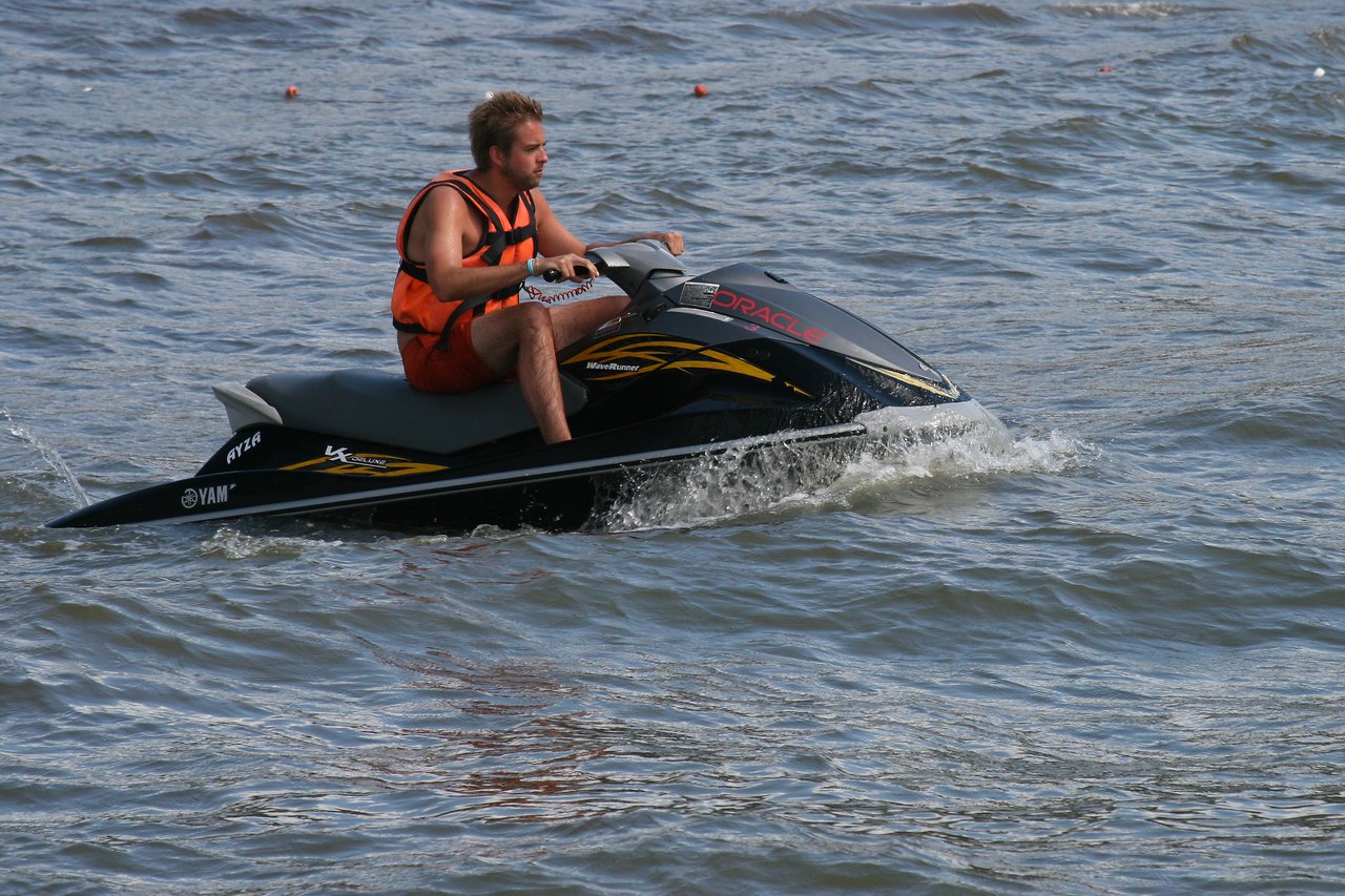 A man wearing an orange life vest rides a black jet ski on the water.