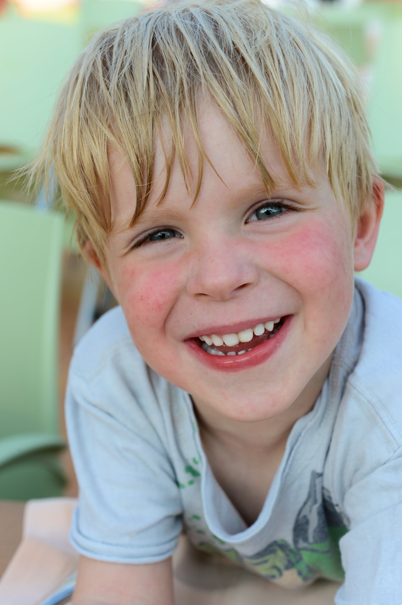 A young child with blond hair and flushed cheeks smiles brightly while looking at the camera.