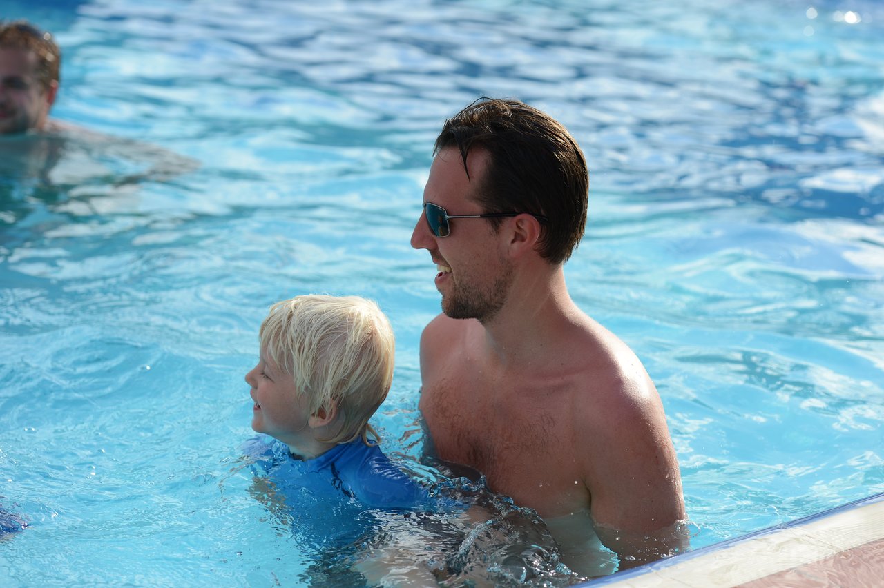 A man and a young child smile while swimming together in a pool.