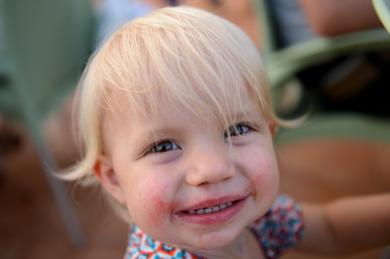 A young child with blonde hair smiles at the camera, showing teeth.