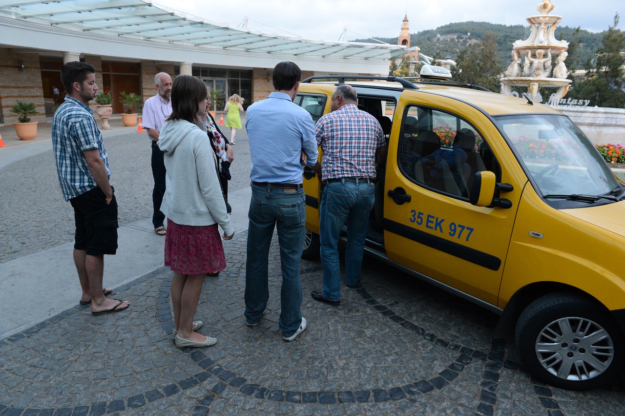 A group of people stands near a yellow taxi as one person loads or adjusts something inside the vehicle.