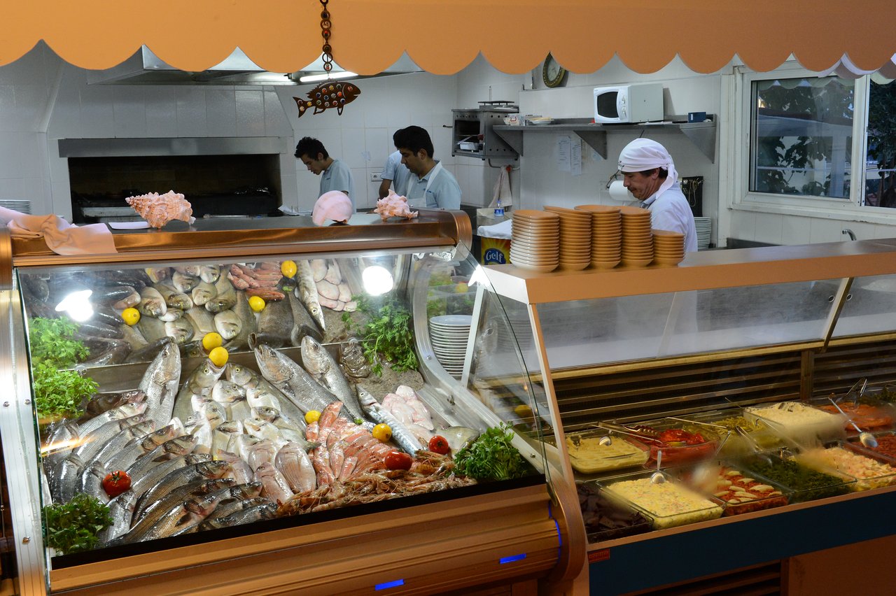 A seafood display with fresh fish and garnishes in a restaurant, with chefs preparing food in the background.