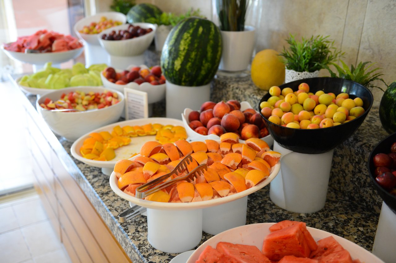A buffet table with various fresh fruits, including watermelon, peaches, and melons, arranged in bowls and plates.