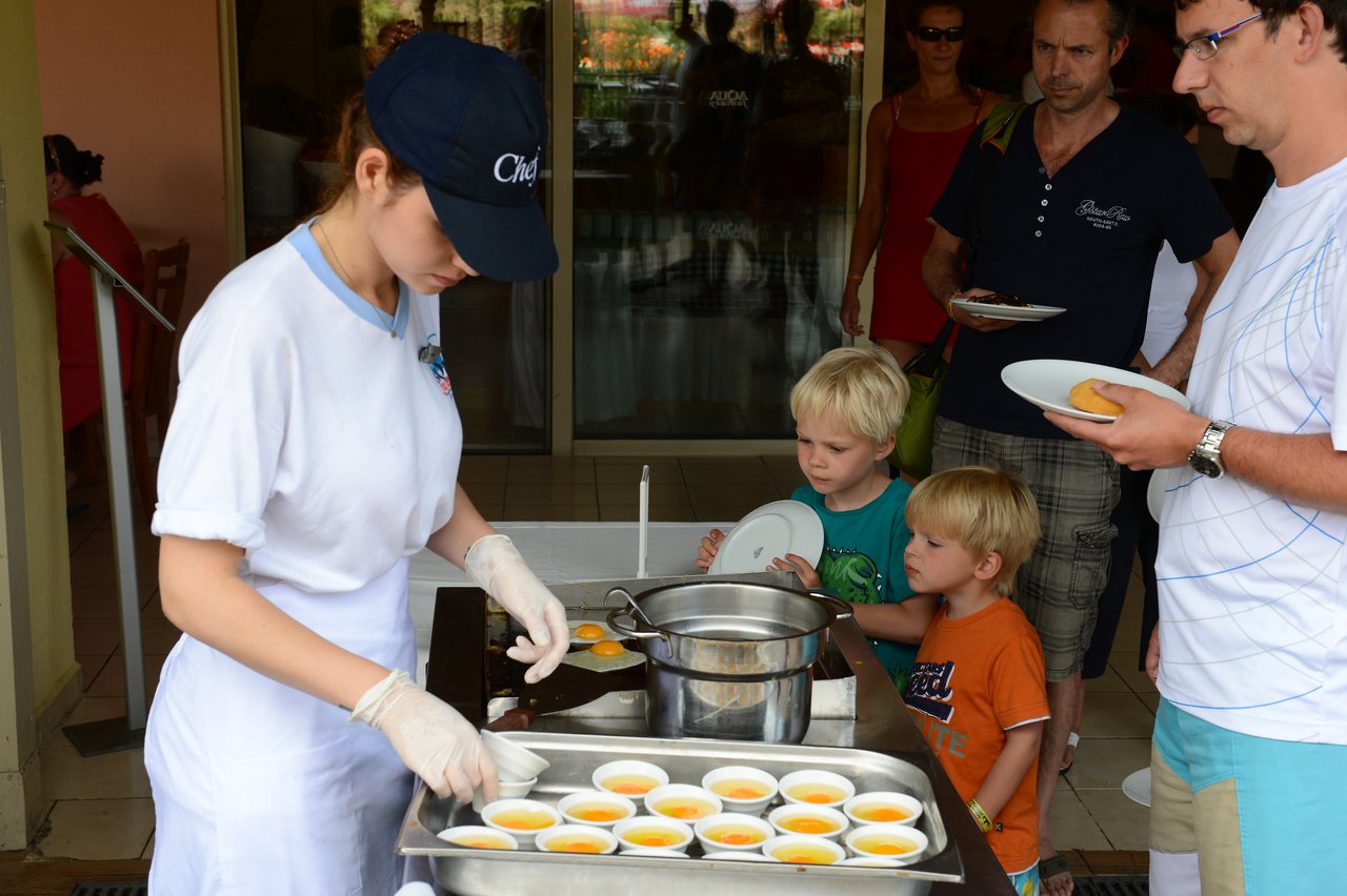 A staff member in a chef's hat serves small bowls of dessert to people waiting in line.