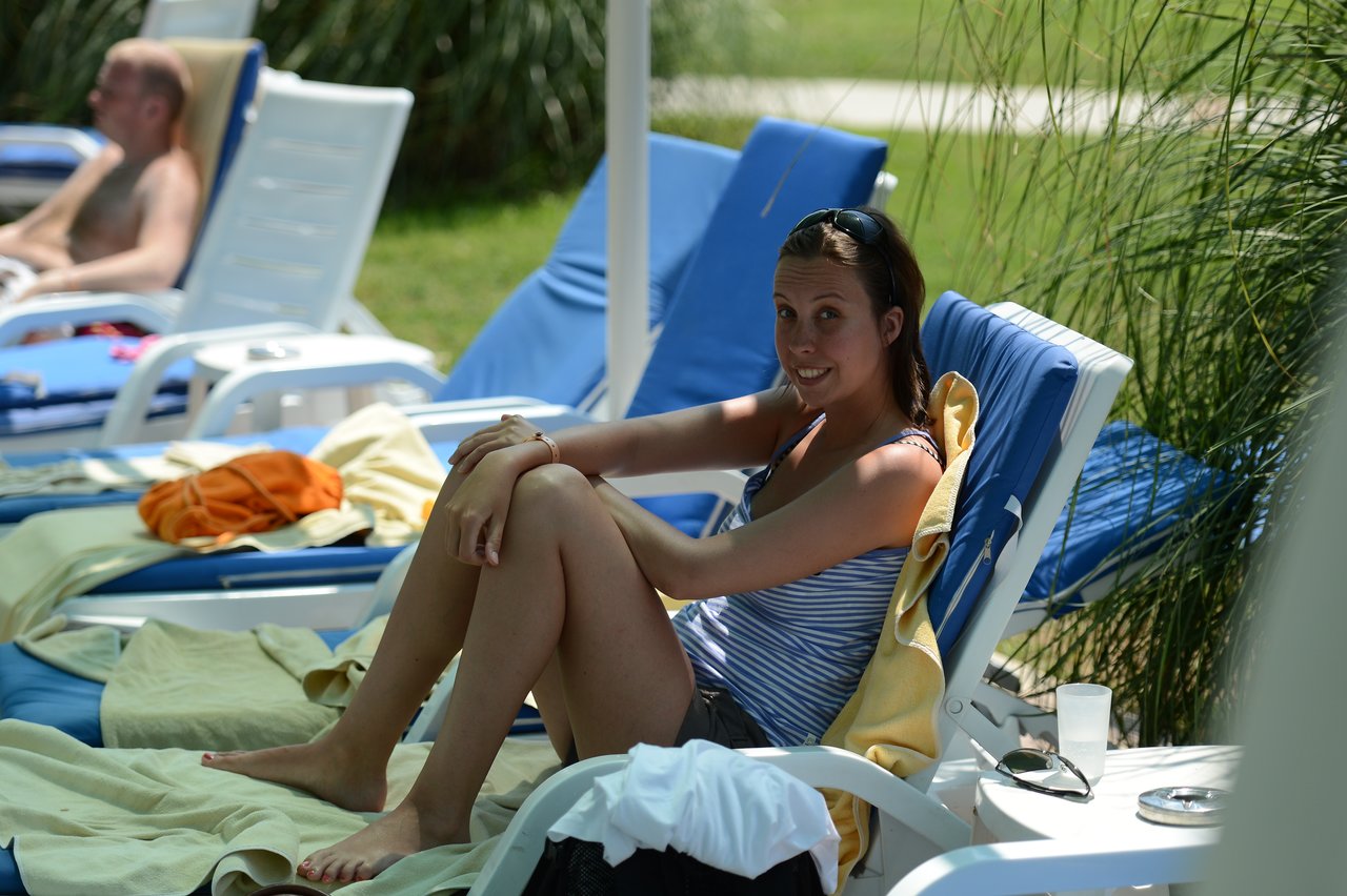 A woman in a striped top sits on a lounge chair by the pool, smiling at the camera.
