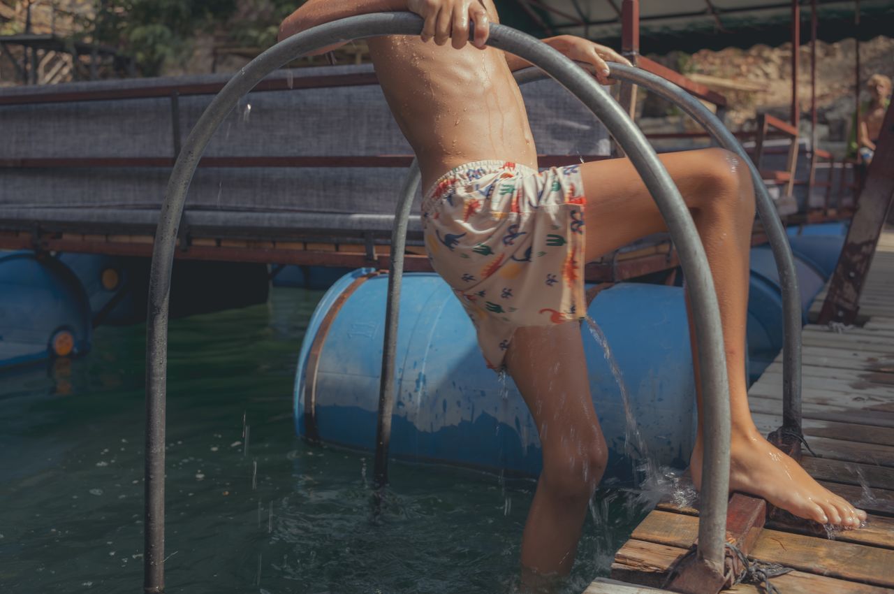 A boy uses a ladder to climb onto a dock from the water.