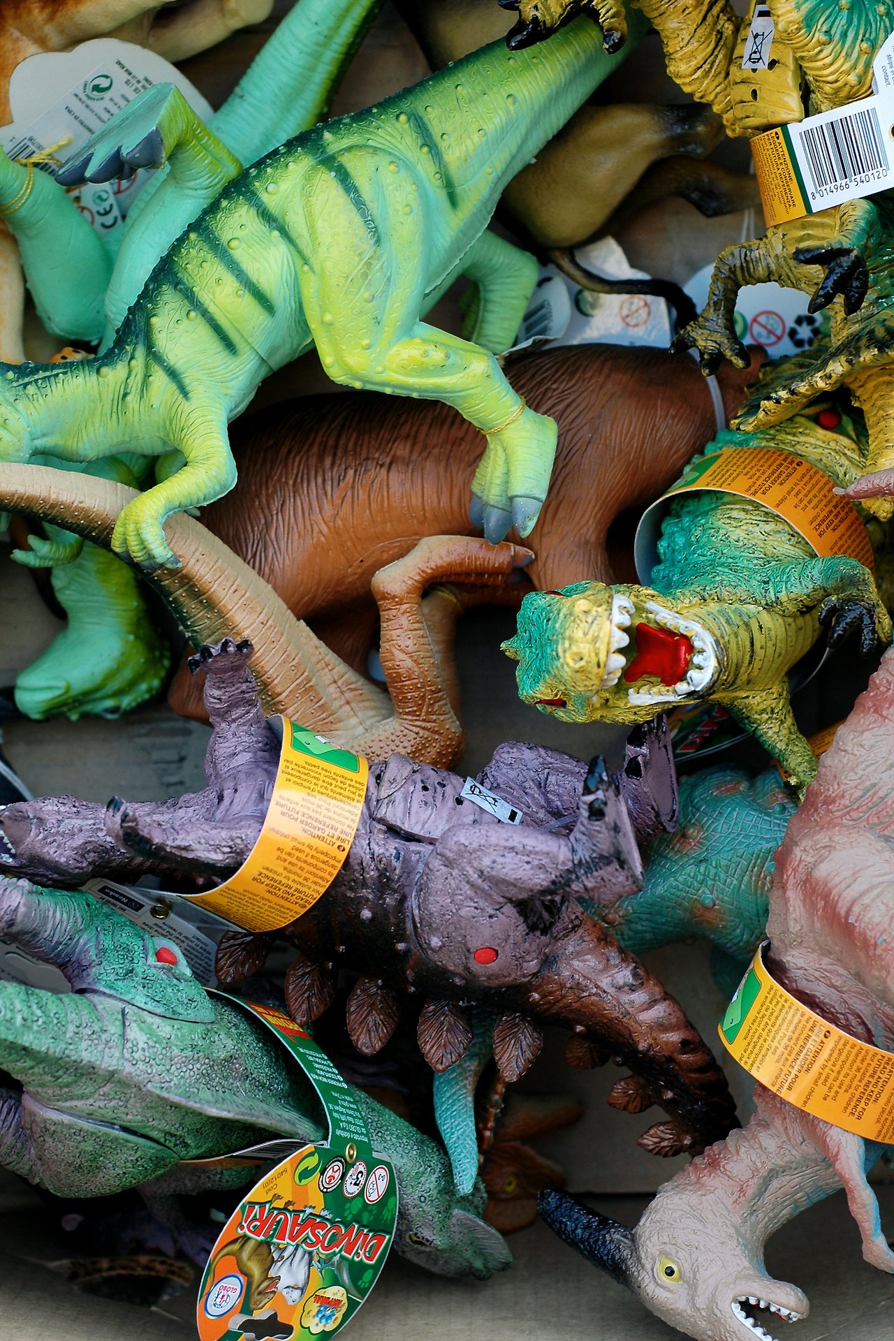 A pile of colorful plastic dinosaur toys with tags, displayed for sale at an outdoor market.