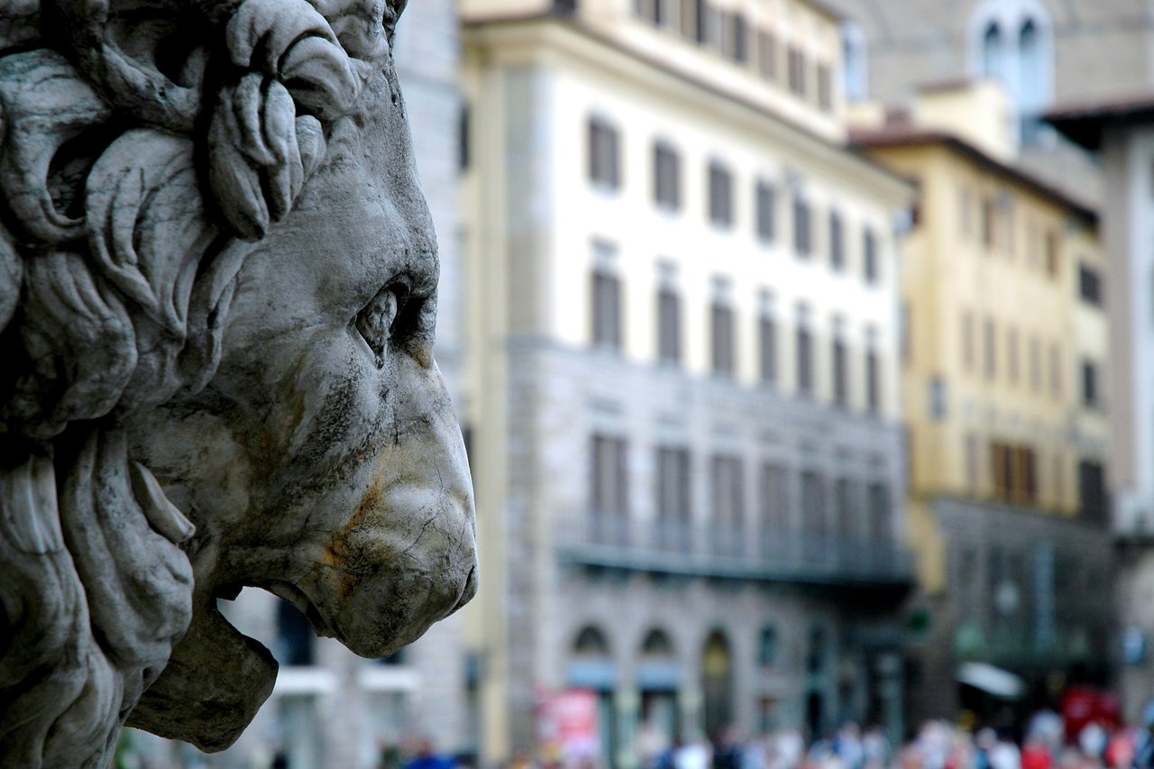Close-up of a stone lion statue in Florence, Italy, with historic buildings in the background.