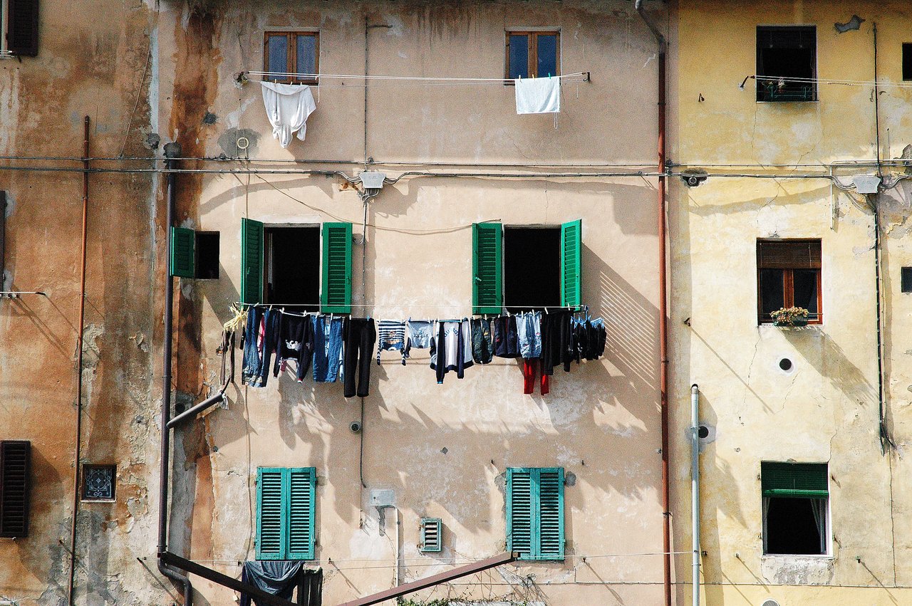 Clothes hanging on a line outside a building with green shutters and weathered walls.