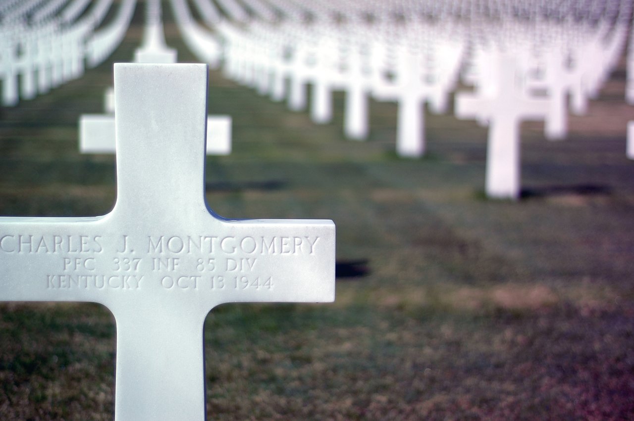 A white cross gravestone in a military cemetery, with rows of similar crosses extending into the distance.