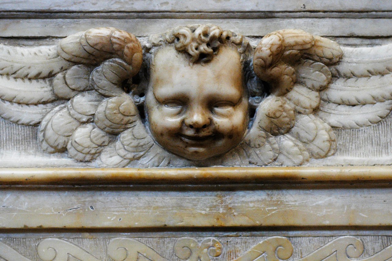 A carved angel ornament with a smiling face and wings inside the Duomo di Siena.