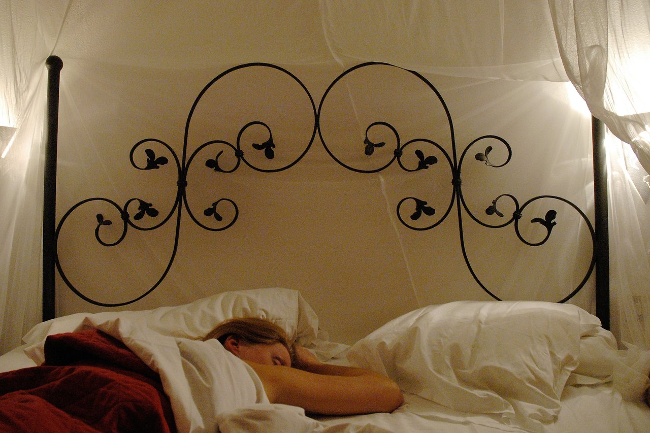 A person is sleeping in a bed with white pillows and sheets, partially covered by a red blanket.