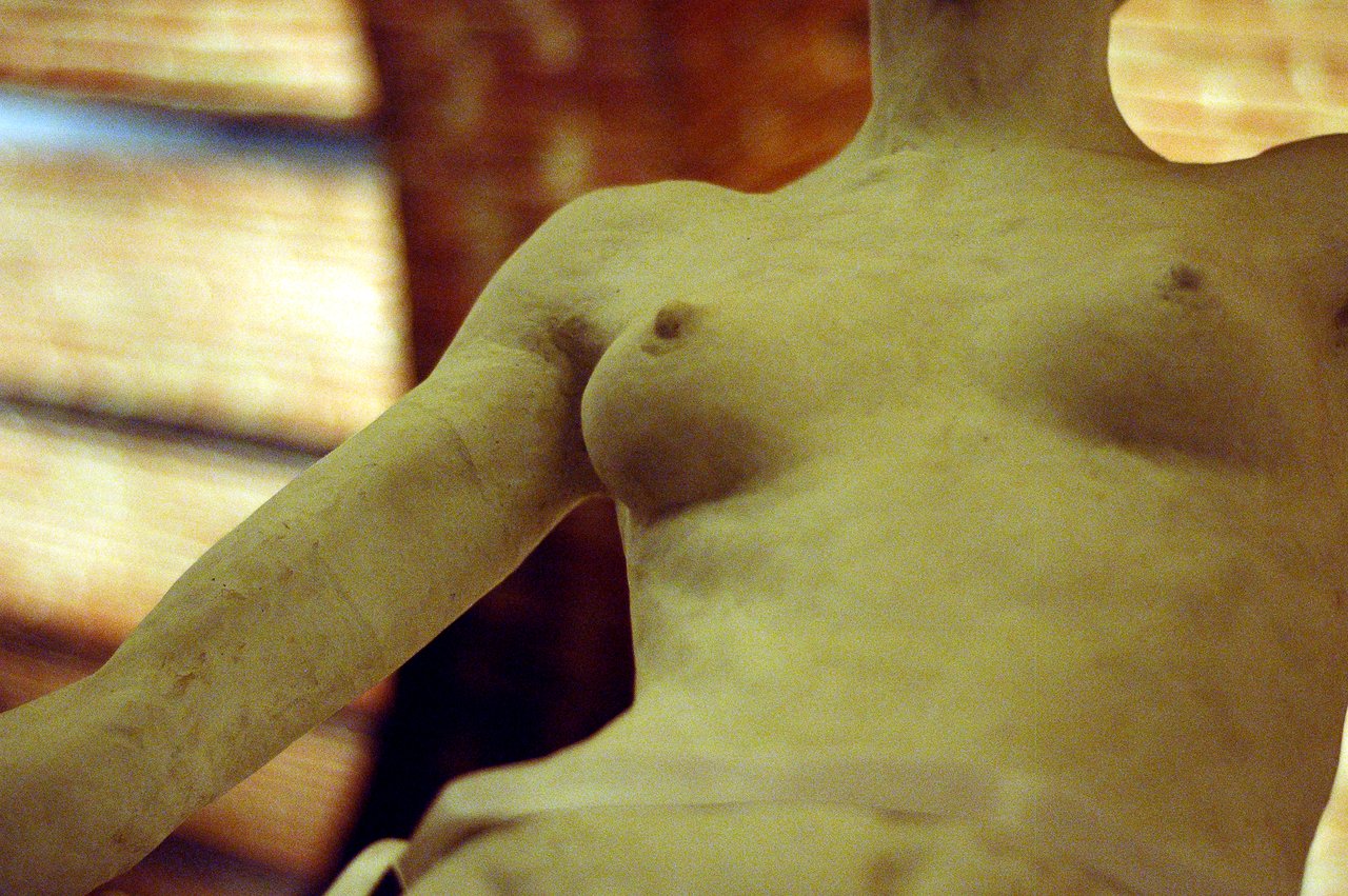 Close-up of a marble statue's upper body, showing the torso and part of the arm in soft lighting.