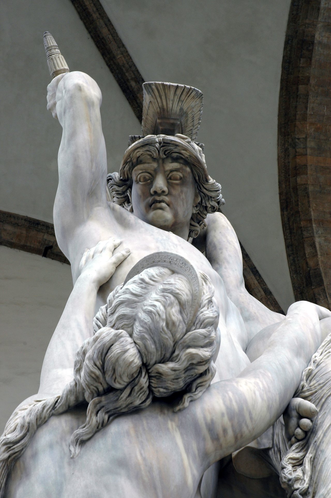 Marble statue of a warrior in a helmet holding a struggling figure, with intense expressions and dynamic movement.