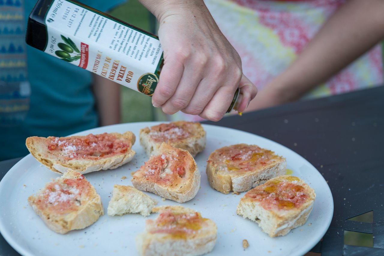 A hand pours olive oil over freshly grilled bruschetta with tomato and salt on a white plate.