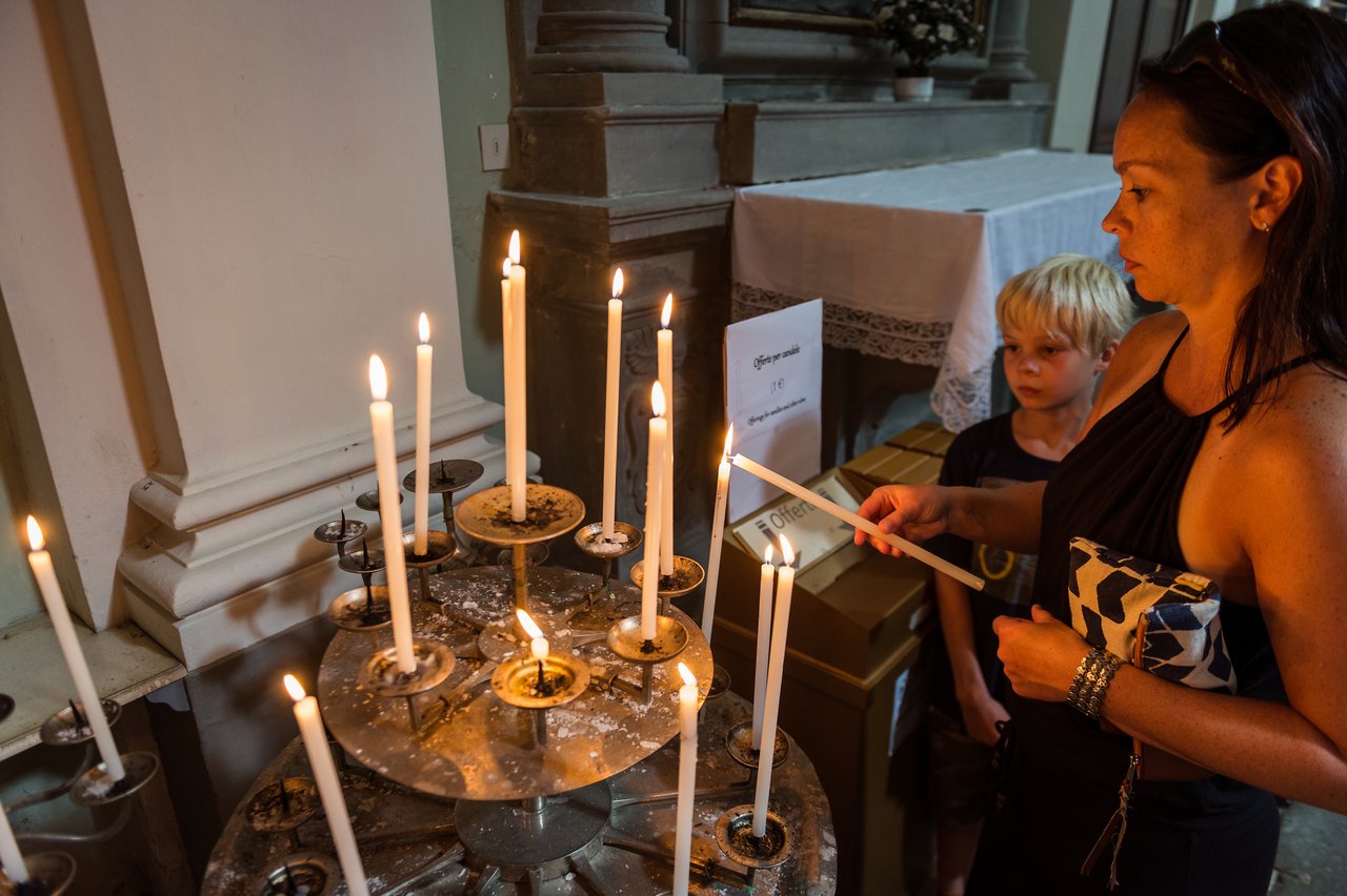 A woman lights a candle in a church while a young boy watches nearby.